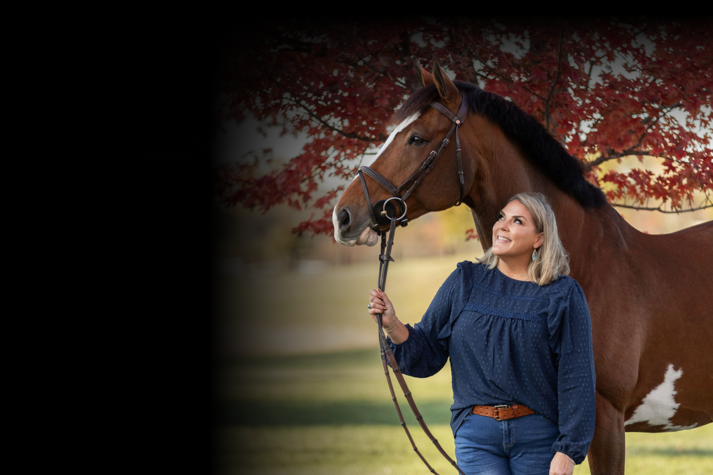 Woman holding a horse by a tree with autumn leaves